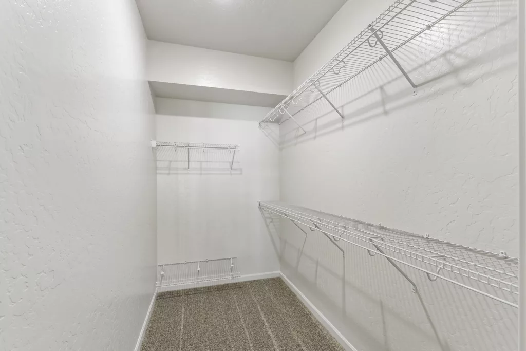A spacious walk-in closet with white wire shelving installed on the walls, and a beige carpeted floor.