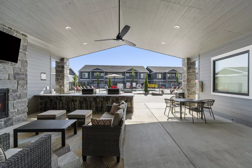 Outdoor patio area with modern seating, a ceiling fan, and a view of a swimming pool and residential buildings in the background.