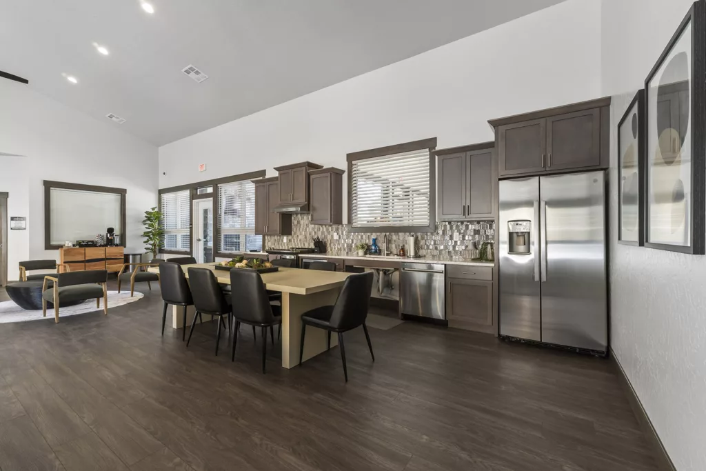 Modern kitchen with stainless steel appliances, dark cabinets, a large dining table with black chairs, and a decorative tile backsplash.