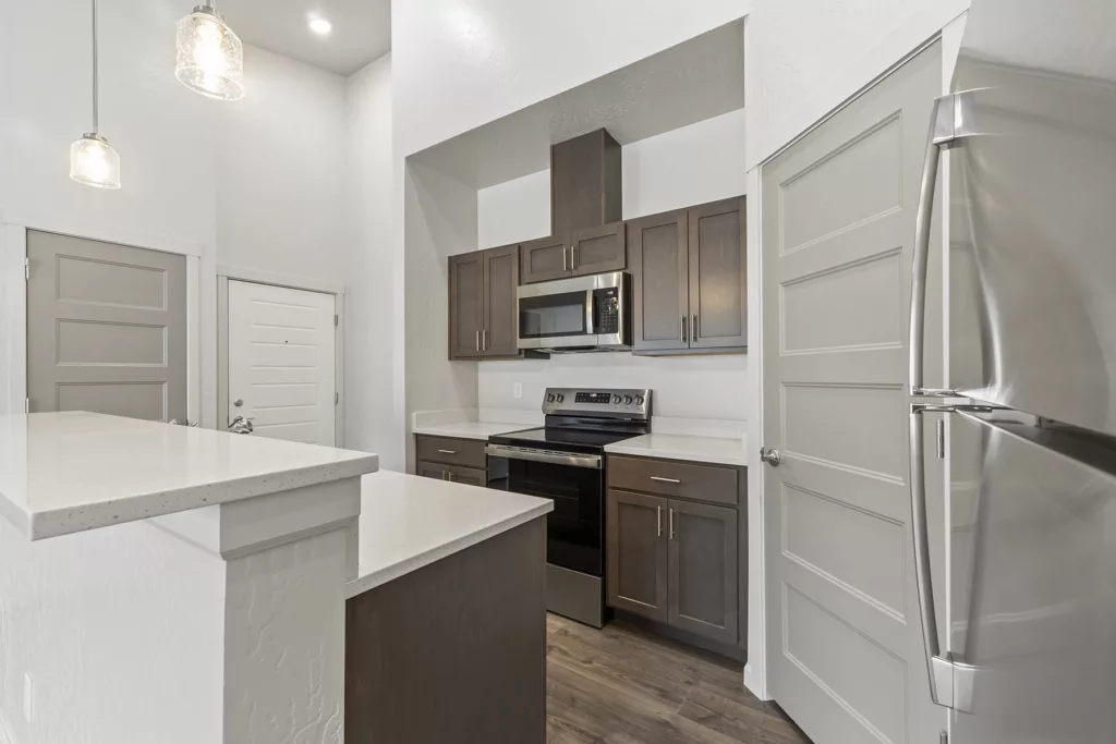 Modern kitchen with dark wood cabinets, stainless steel appliances, white countertops, and pendant lighting, featuring a microwave and electric stove.