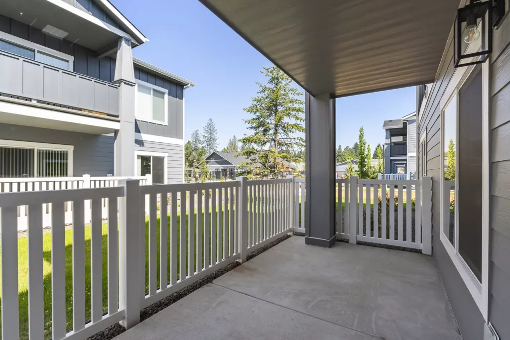 Covered patio with white fence and view of modern houses with gray siding and green lawns.