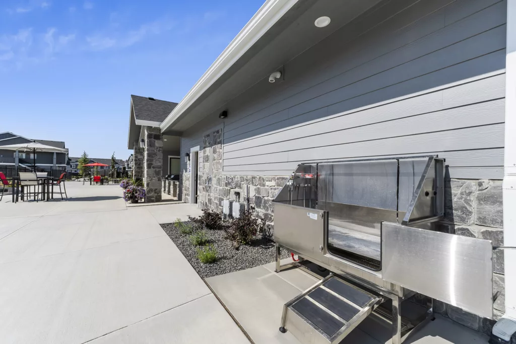 Outdoor patio area with patio furniture and a stainless steel dog wash station, adjacent to a building with stone and siding exterior.