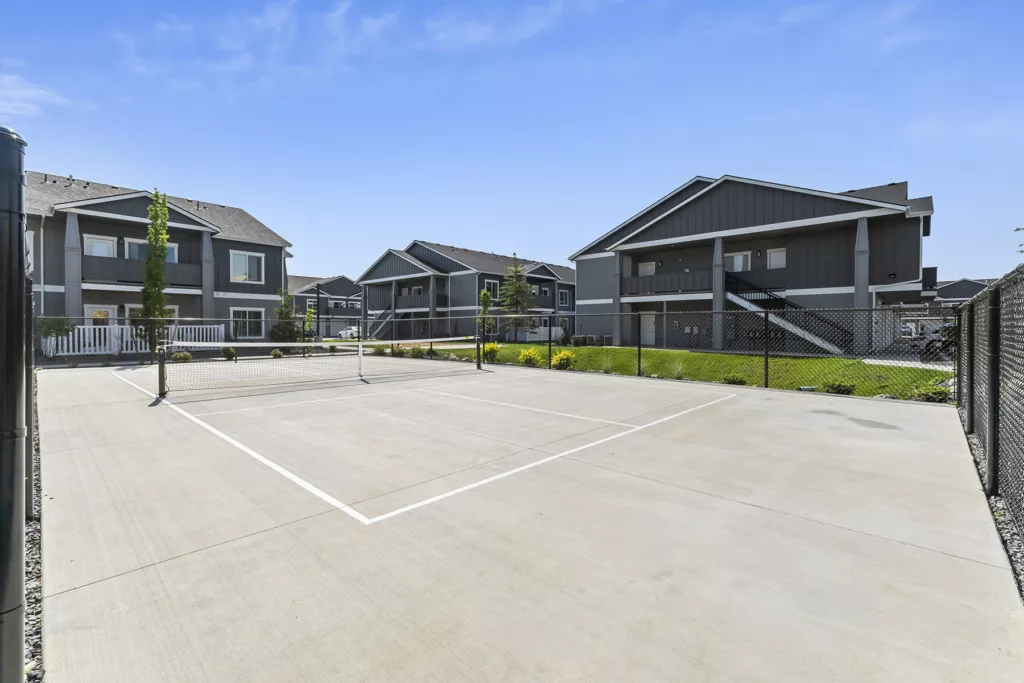 An outdoor tennis court surrounded by modern apartment buildings under a clear blue sky.