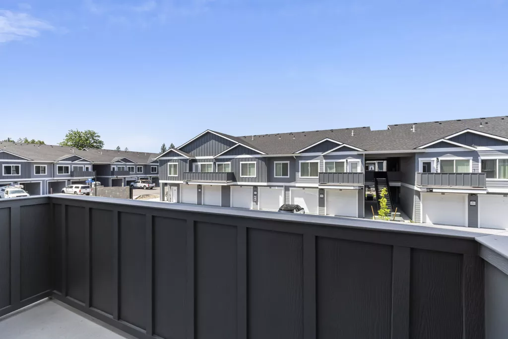 View from a balcony overlooking a row of modern townhouses with dark gray siding and white doors, under a clear blue sky.